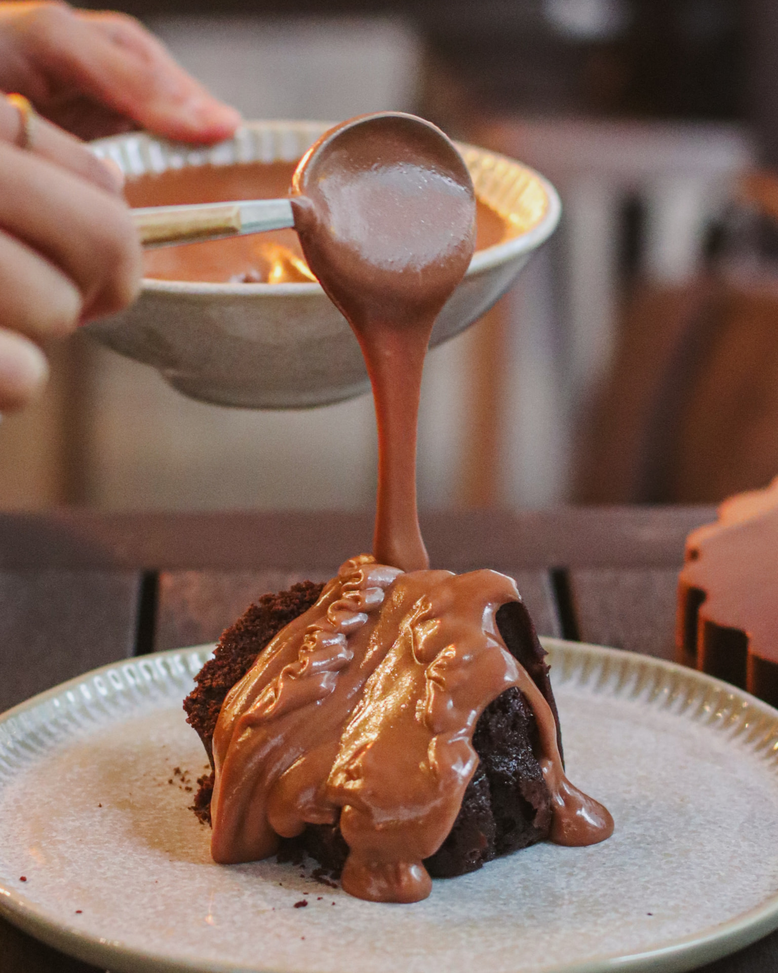 Calda de chocolate sendo servida sobre uma fatia de torta
